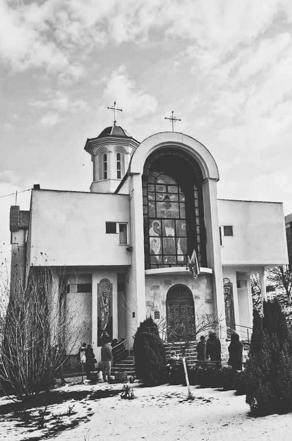 Black and white image of a decorative cake with a heart shape on top, placed on a plate on white bedding with a fork beside it.